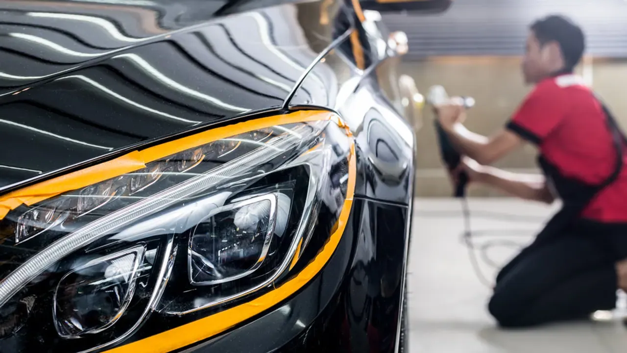 A detailer working across a masked car panel in a bright workshop