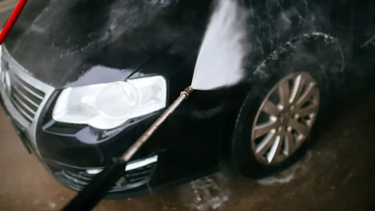 A pressure washer rinsing the wheel area of a dark car