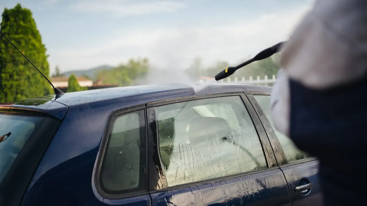 A person washing a blue car in a residential driveway