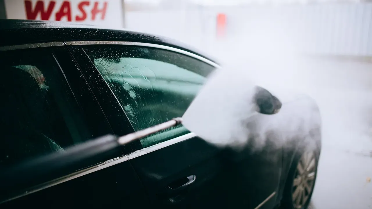 Water and foam spraying across a dark car at a wash bay