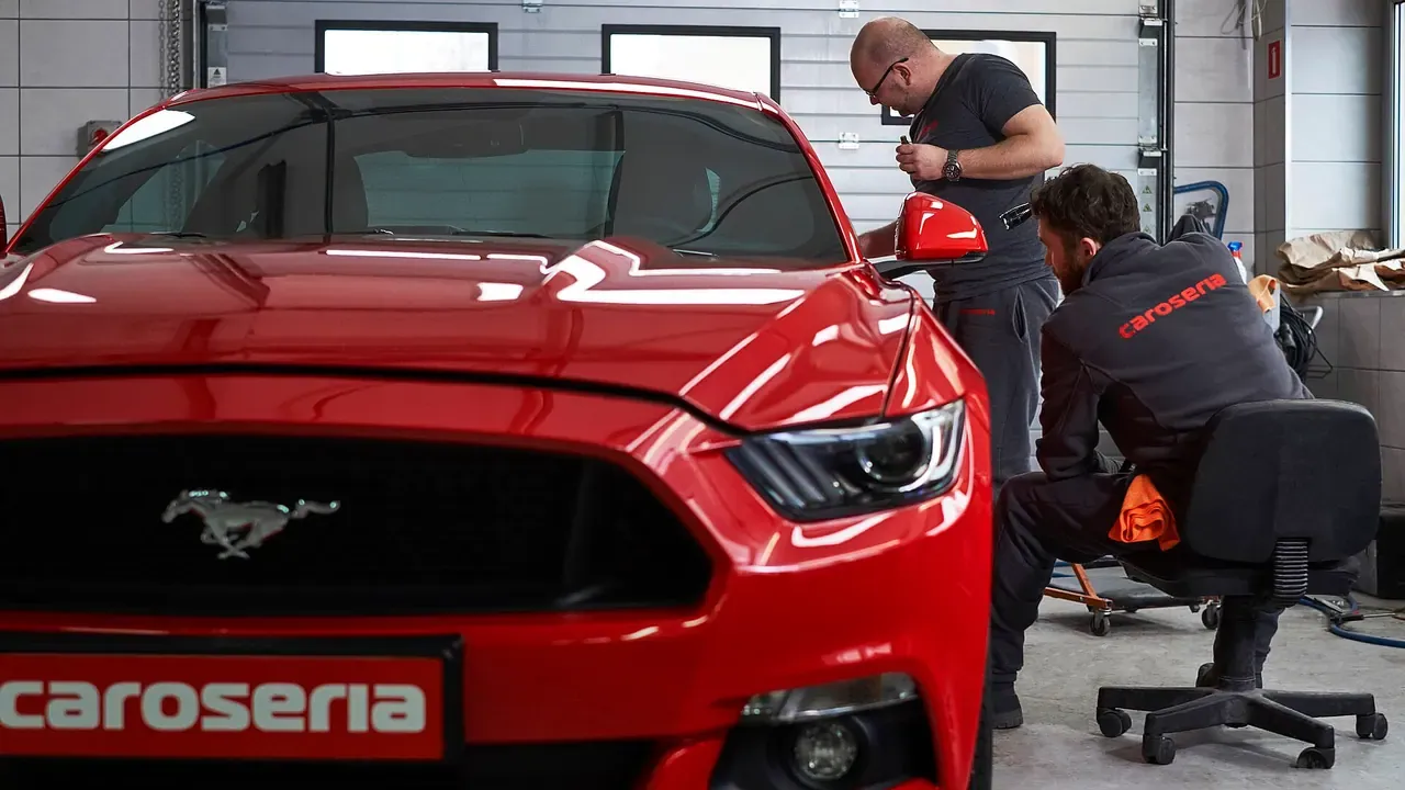 A detailer machine-polishing the hood of a red car