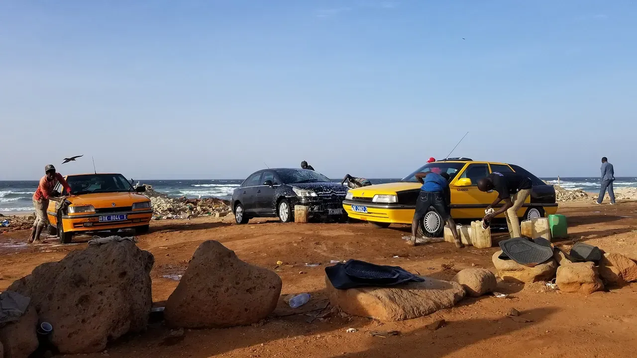 Several people hand-washing cars at an outdoor taxi stand