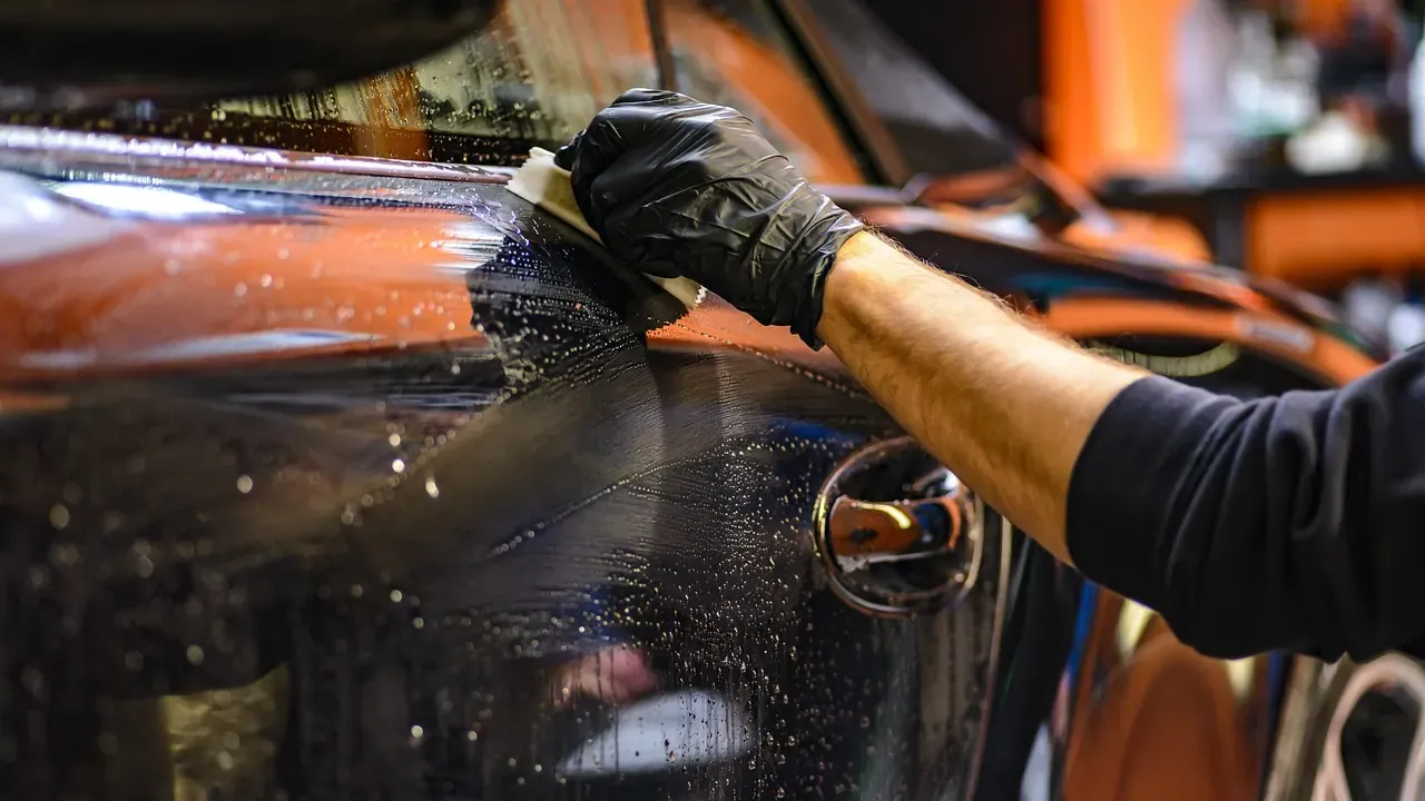 A detailer polishing the side of a dark car