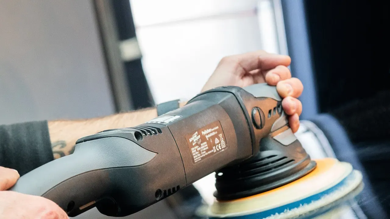 A detailer polishing a dark vehicle panel with a machine polisher