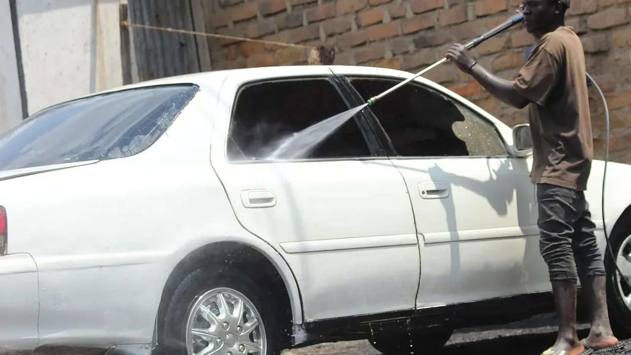 A man rinsing the side of a white car outdoors