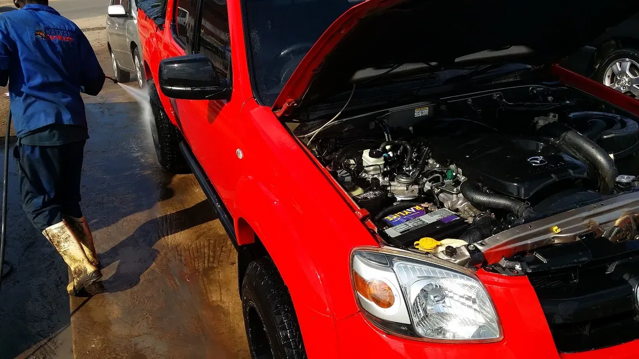 A red car with its hood open during an outdoor wash