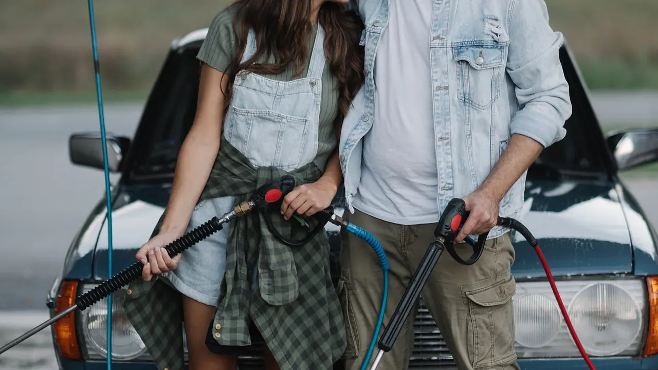 Two people holding wash hoses beside a car at an outdoor wash