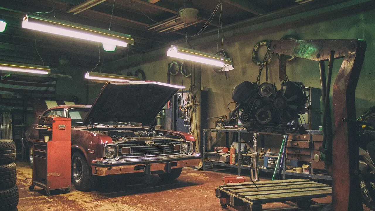 A vintage red car and suspended engine inside a repair shop