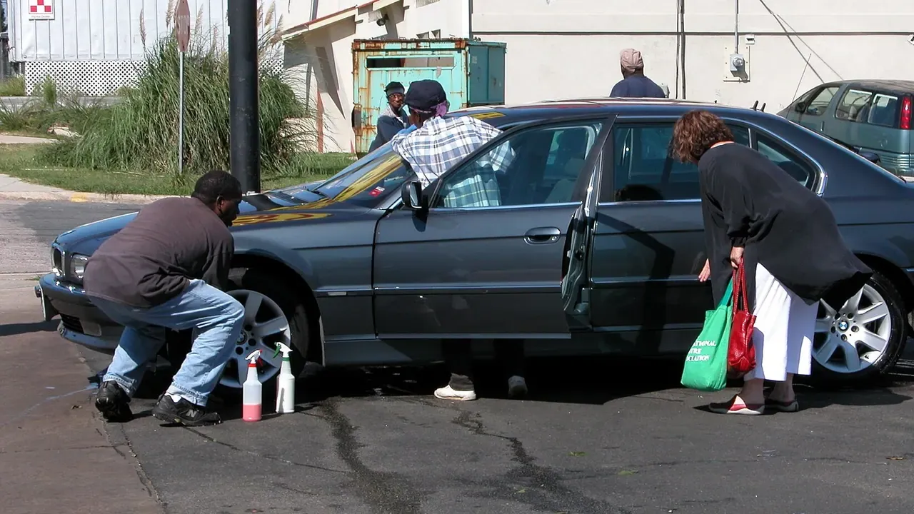 Two people hand-washing a dark sedan at an outdoor car wash