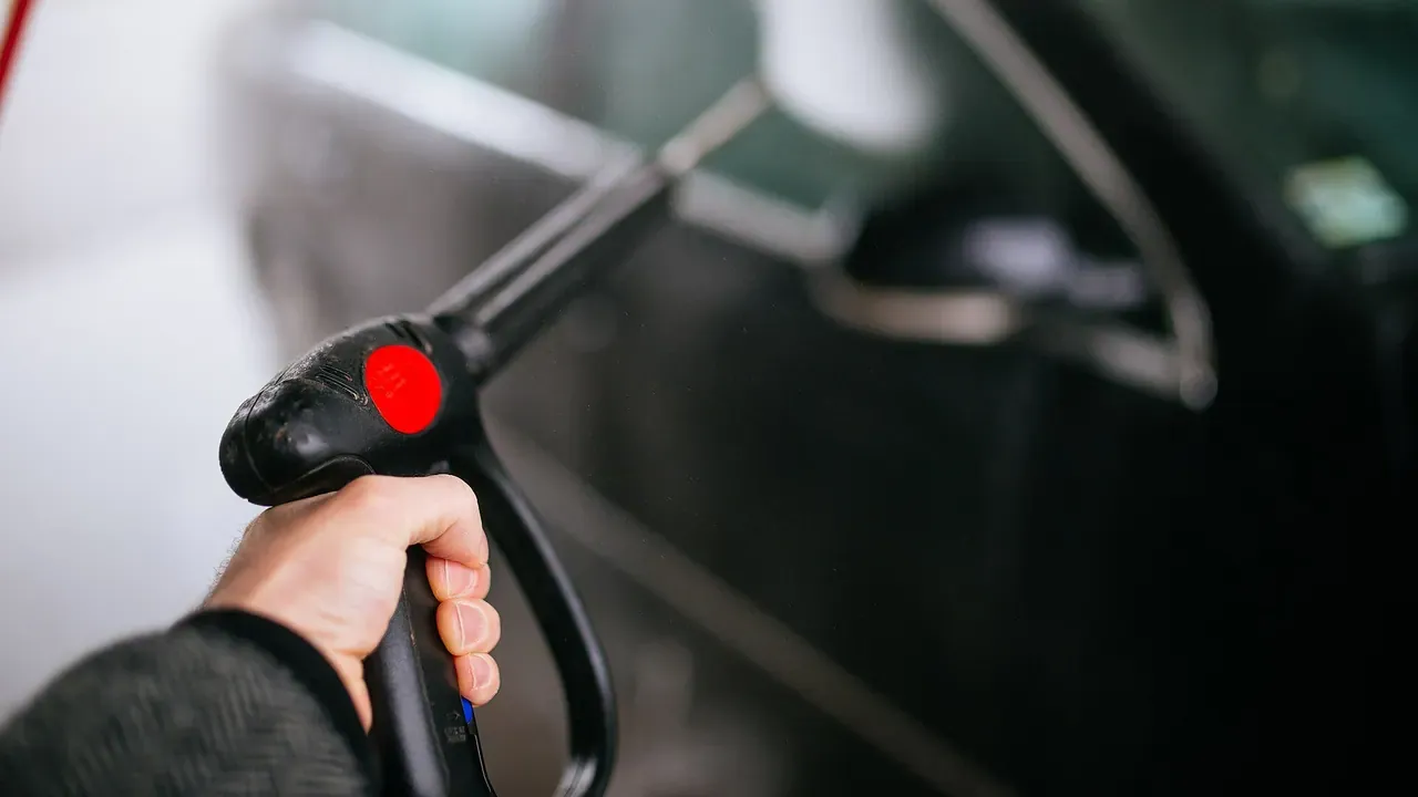 A pressure-washer nozzle spraying the side of a dark car