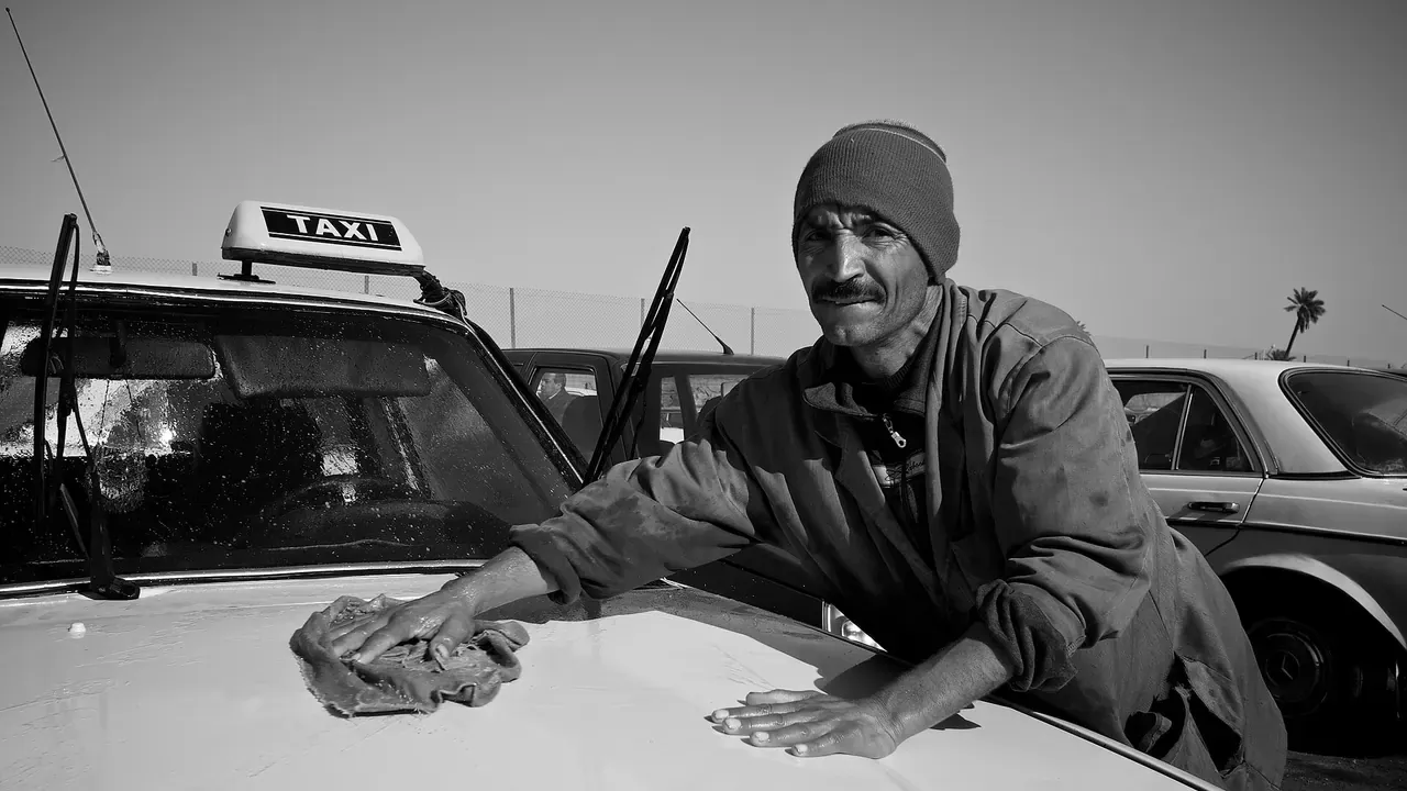 A man wiping a car beside a row of parked vehicles
